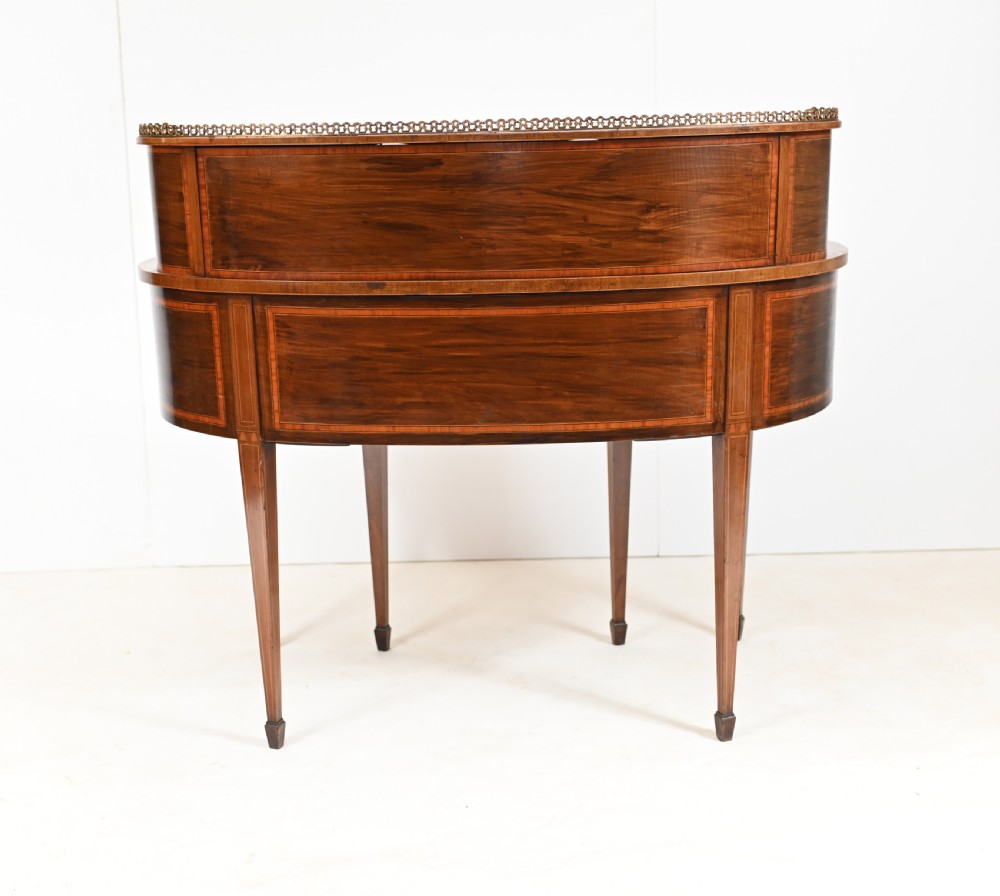 An Edwardian mahogany kidney-shaped writing desk featuring a brass gallery top, inlaid drawers, black leather writing inserts, and tapered legs. View XIII