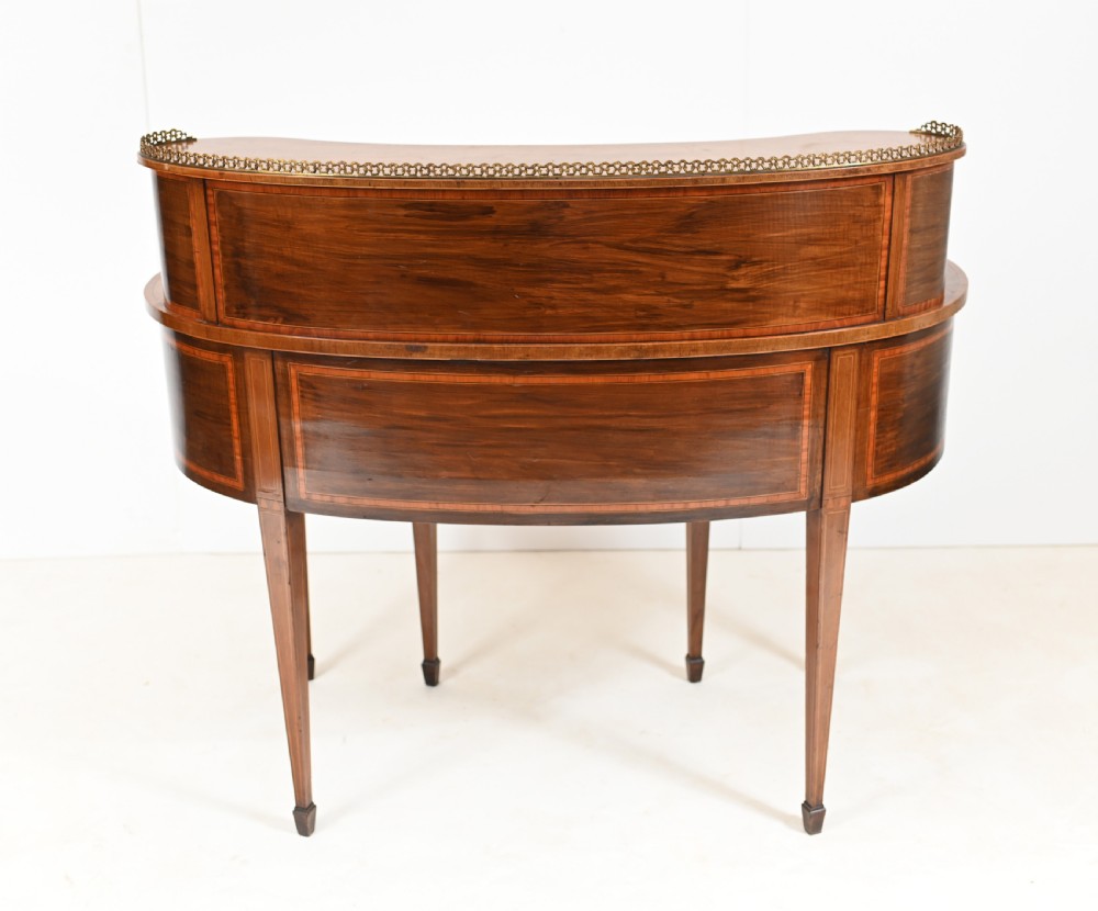 An Edwardian mahogany kidney-shaped writing desk featuring a brass gallery top, inlaid drawers, black leather writing inserts, and tapered legs. View XIV