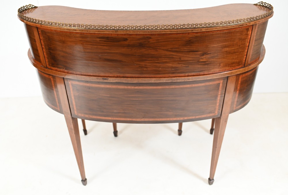 An Edwardian mahogany kidney-shaped writing desk featuring a brass gallery top, inlaid drawers, black leather writing inserts, and tapered legs. View XV