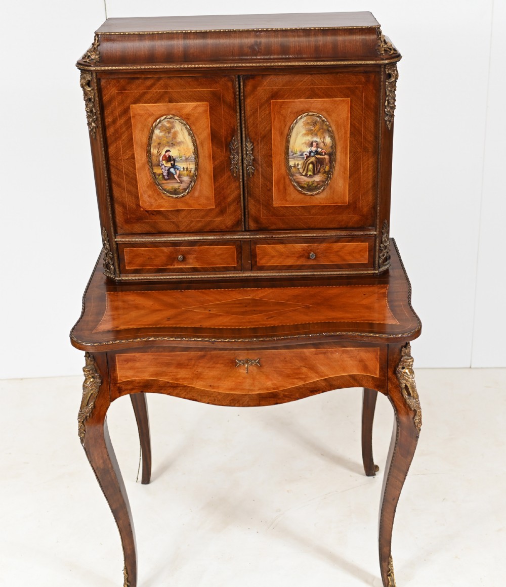 A French Louis XV style kingwood bonheur de jour desk featuring two upper cabinet doors inset with oval painted porcelain plaques, ornate metal mounts, and cabriole legs. View II