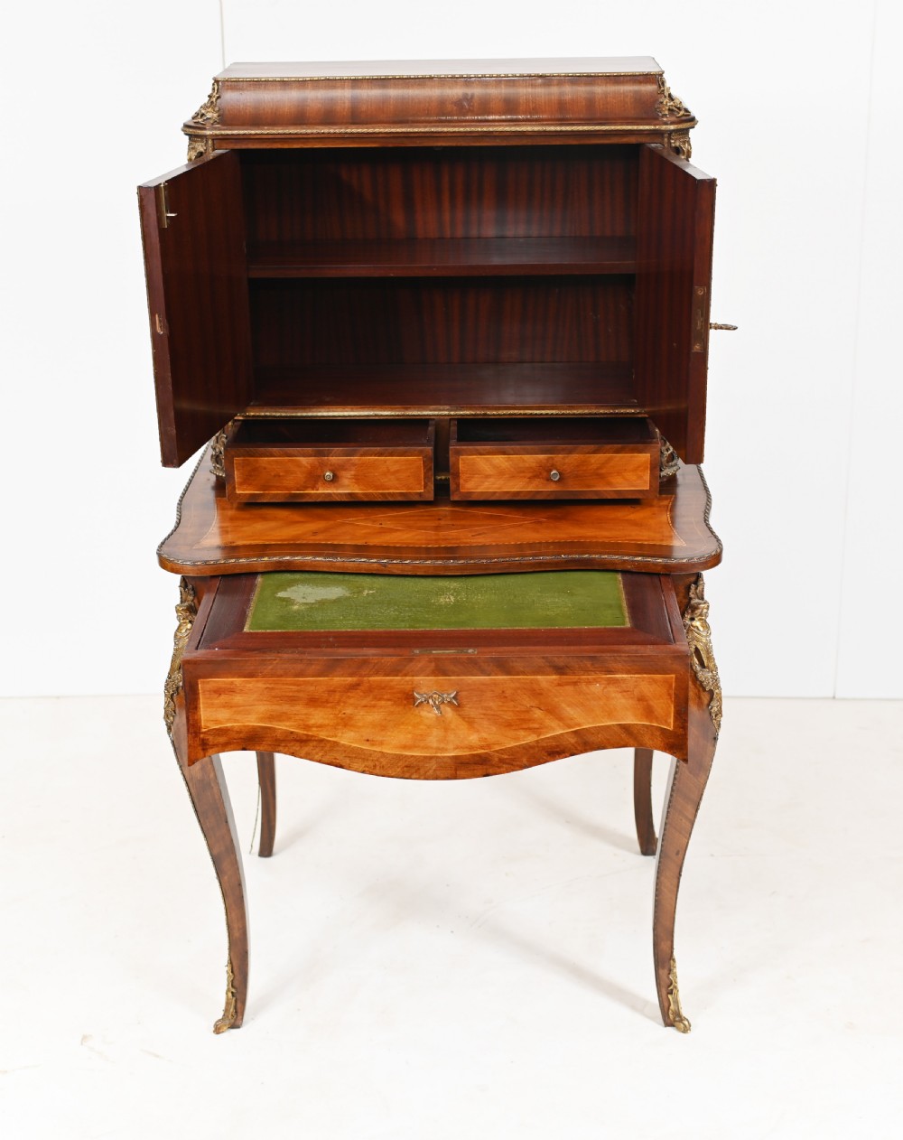 A French Louis XV style kingwood bonheur de jour desk featuring two upper cabinet doors inset with oval painted porcelain plaques, ornate metal mounts, and cabriole legs. View VI