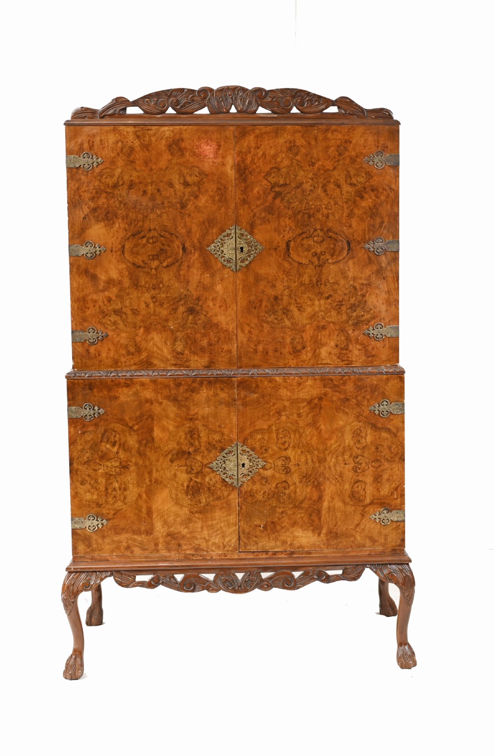 A two-tier Art Deco burr walnut cocktail cabinet featuring decorative brass strap hinges, lock plates, carved cresting, and cabriole legs.