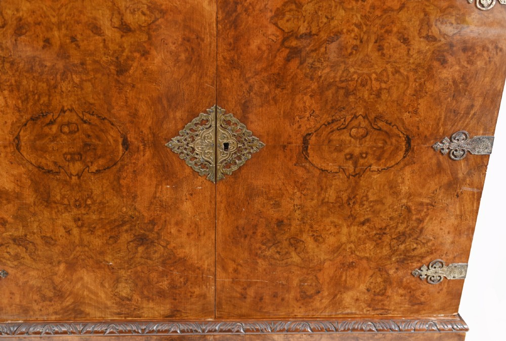 A two-tier Art Deco burr walnut cocktail cabinet featuring decorative brass strap hinges, lock plates, carved cresting, and cabriole legs. View III