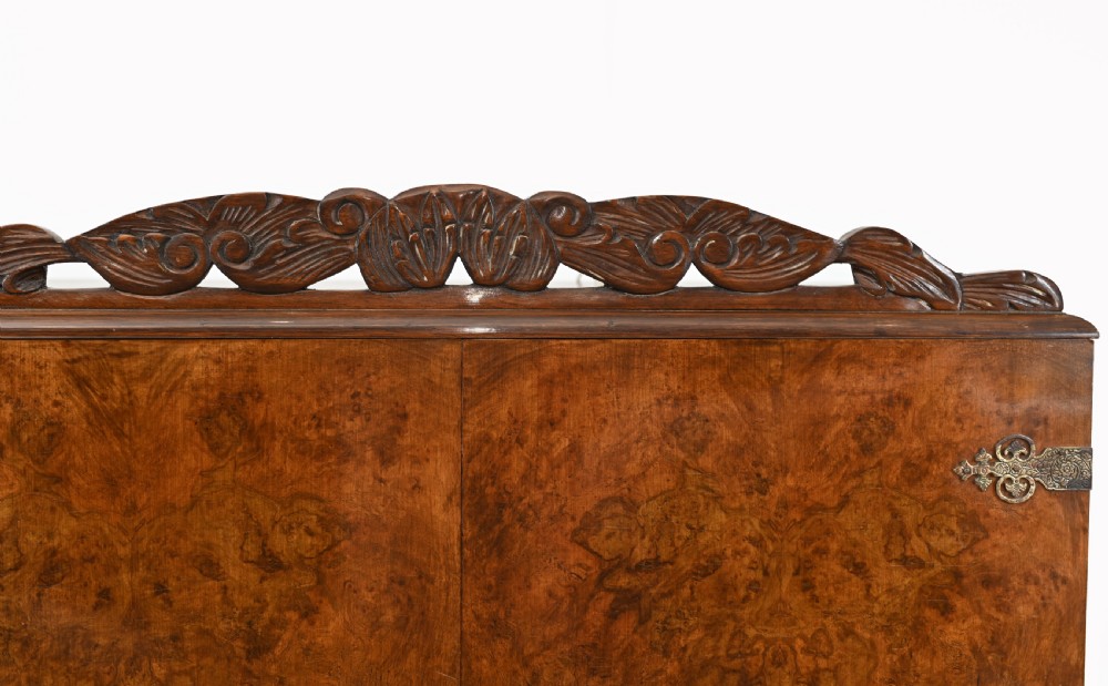 A two-tier Art Deco burr walnut cocktail cabinet featuring decorative brass strap hinges, lock plates, carved cresting, and cabriole legs. View IV