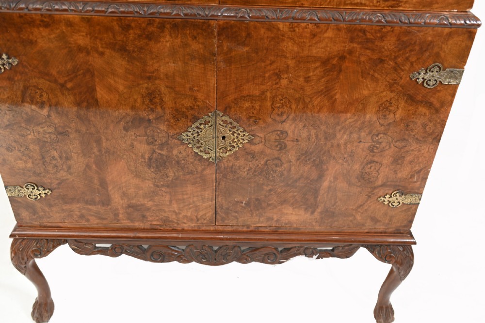 A two-tier Art Deco burr walnut cocktail cabinet featuring decorative brass strap hinges, lock plates, carved cresting, and cabriole legs. View V