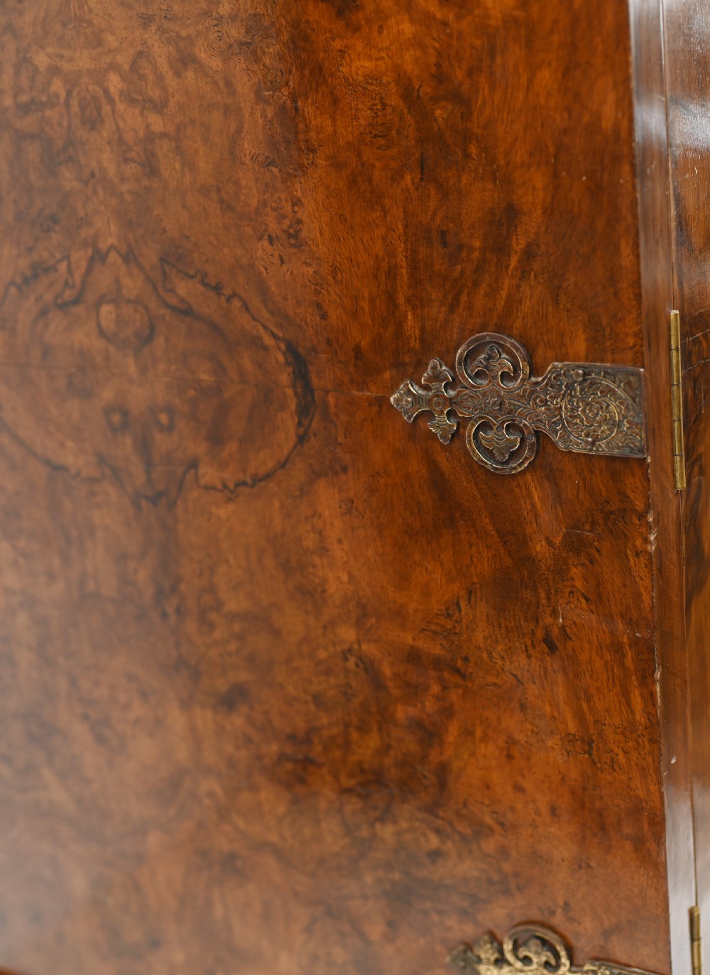 A two-tier Art Deco burr walnut cocktail cabinet featuring decorative brass strap hinges, lock plates, carved cresting, and cabriole legs. View XI