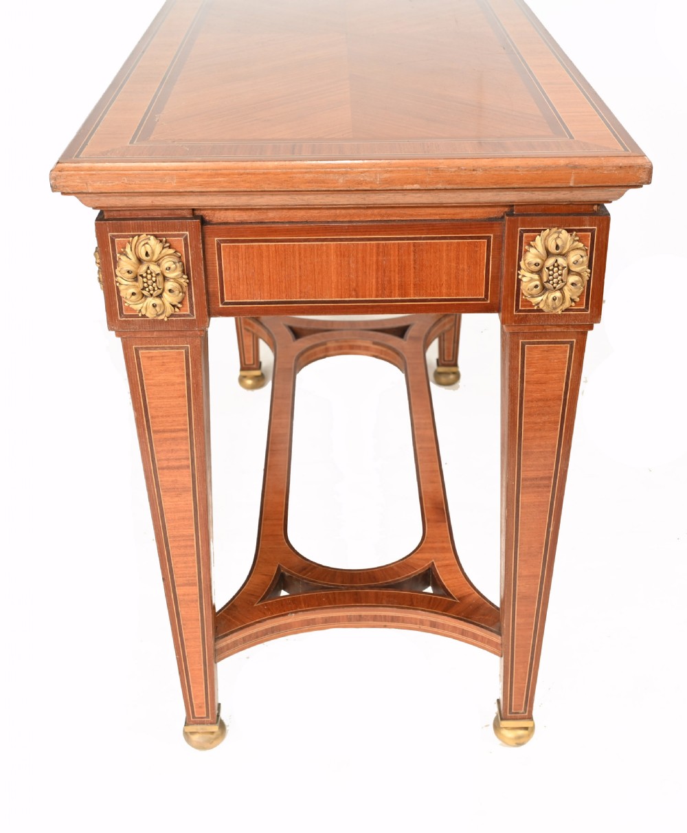 A pair of French Empire style mahogany console tables featuring satinwood crossbanding, gilt-bronze rosette mounts, and curved lower stretchers. View IX