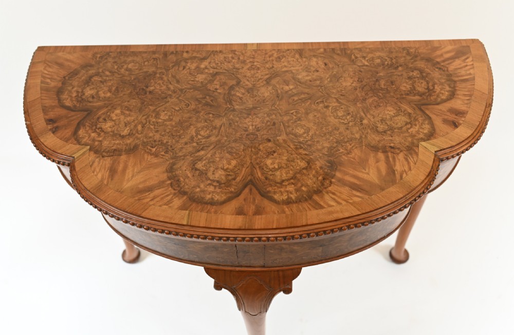 A Queen Anne style burr walnut fold-over card table featuring a scalloped demilune top, bead moulding, and four cabriole legs ending in pad feet. View III