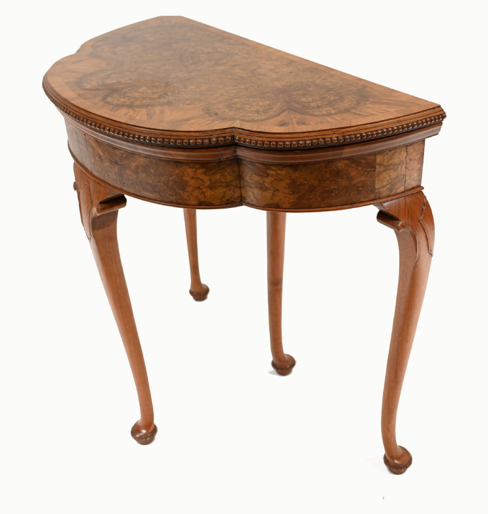 A Queen Anne style burr walnut fold-over card table featuring a scalloped demilune top, bead moulding, and four cabriole legs ending in pad feet. View IV