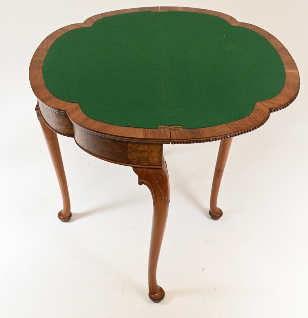 A Queen Anne style burr walnut fold-over card table featuring a scalloped demilune top, bead moulding, and four cabriole legs ending in pad feet. View VI
