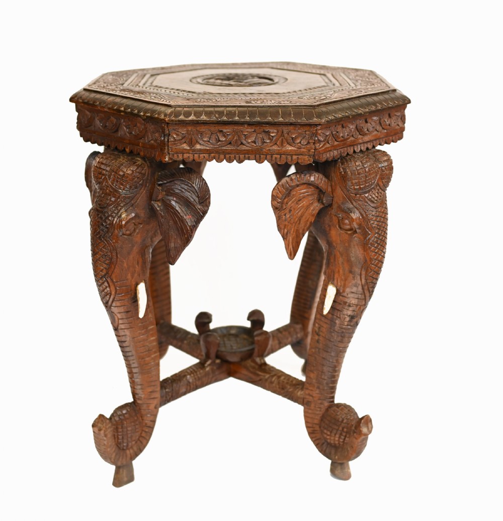 An octagonal carved wooden side table featuring three legs sculpted in the shape of elephant heads with trunks curving down to form the feet.
