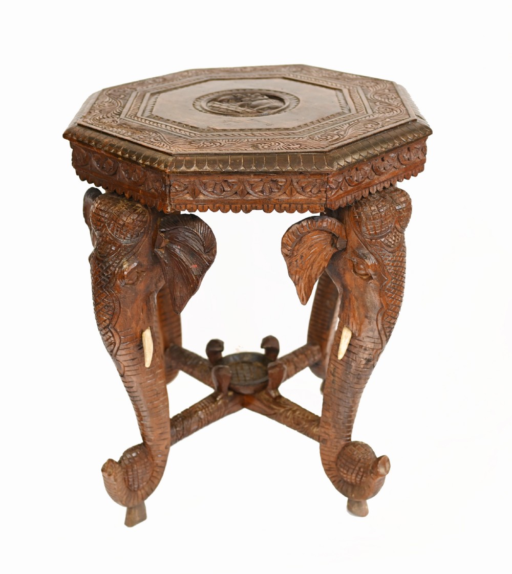 An octagonal carved wooden side table featuring three legs sculpted in the shape of elephant heads with trunks curving down to form the feet. View II
