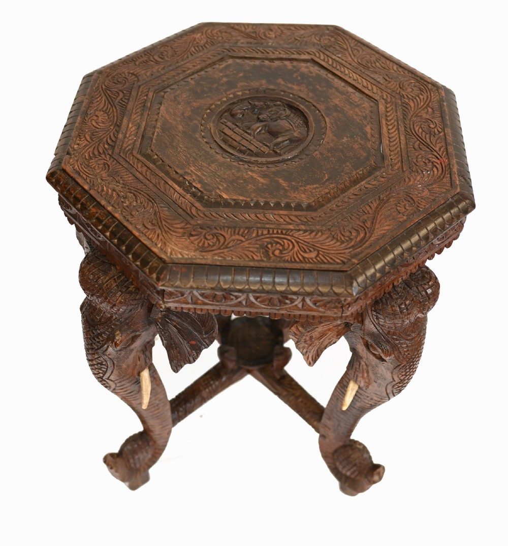 An octagonal carved wooden side table featuring three legs sculpted in the shape of elephant heads with trunks curving down to form the feet. View III