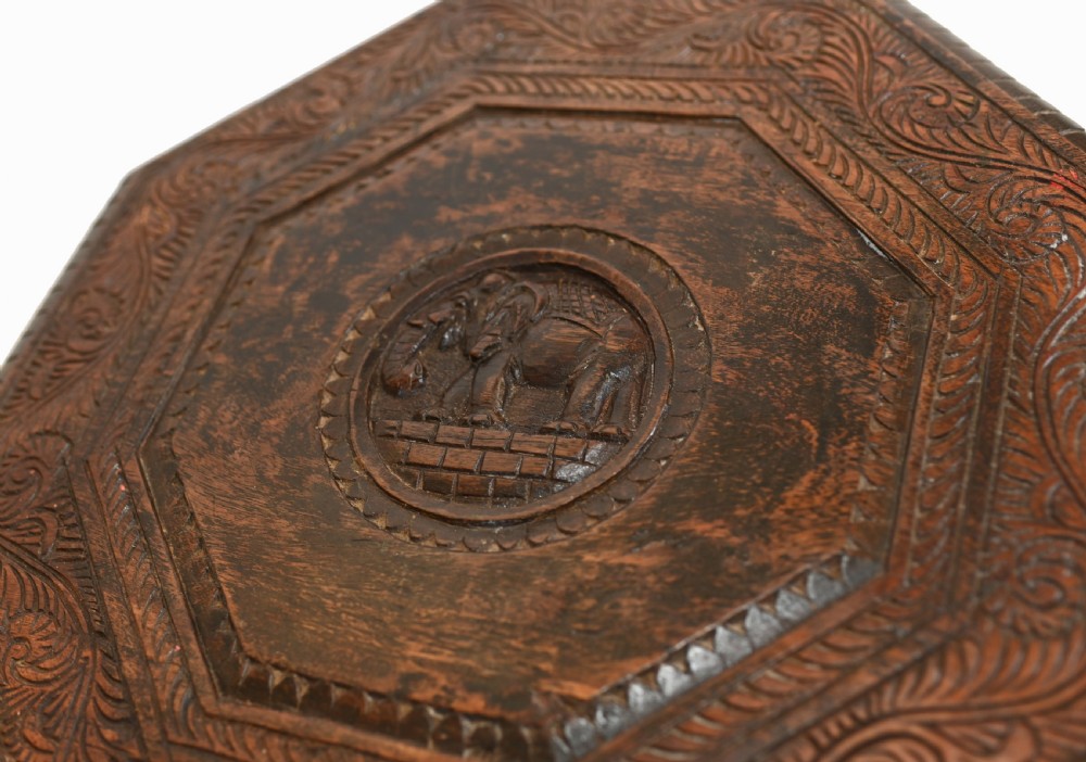 An octagonal carved wooden side table featuring three legs sculpted in the shape of elephant heads with trunks curving down to form the feet. View IV