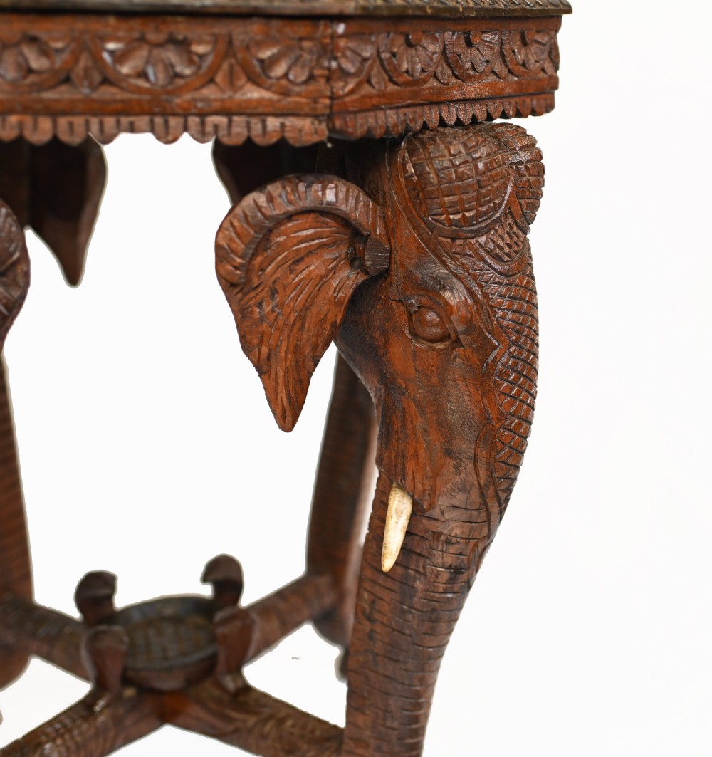An octagonal carved wooden side table featuring three legs sculpted in the shape of elephant heads with trunks curving down to form the feet. View V