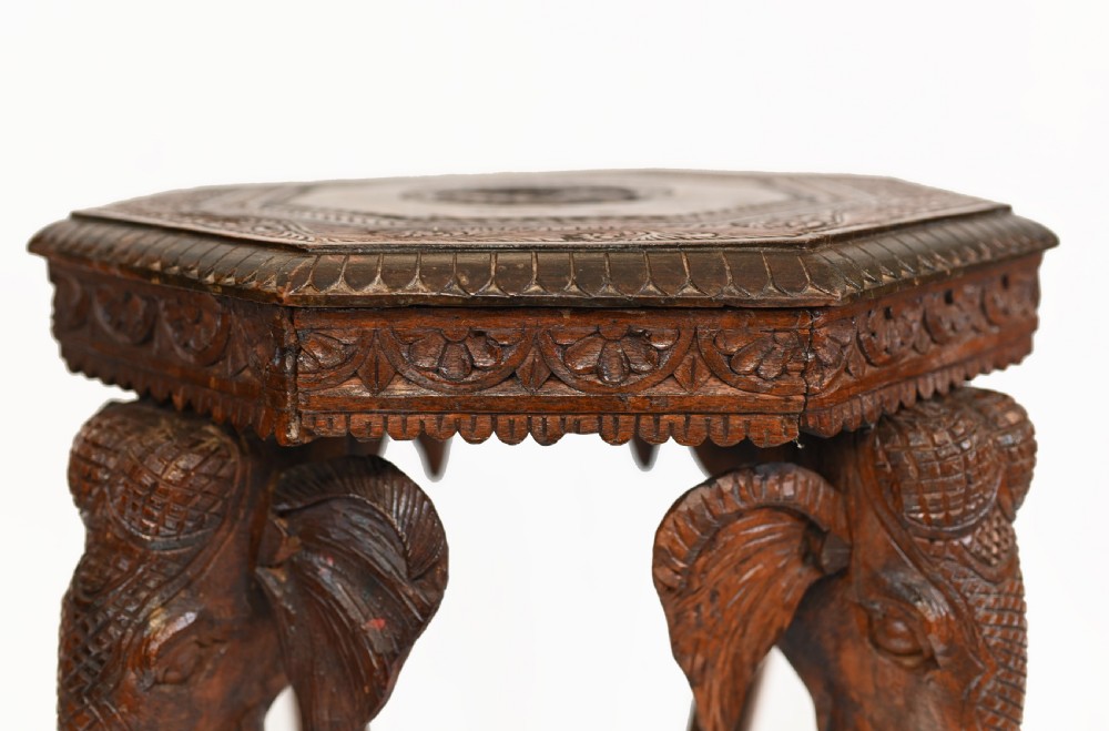 An octagonal carved wooden side table featuring three legs sculpted in the shape of elephant heads with trunks curving down to form the feet. View VI