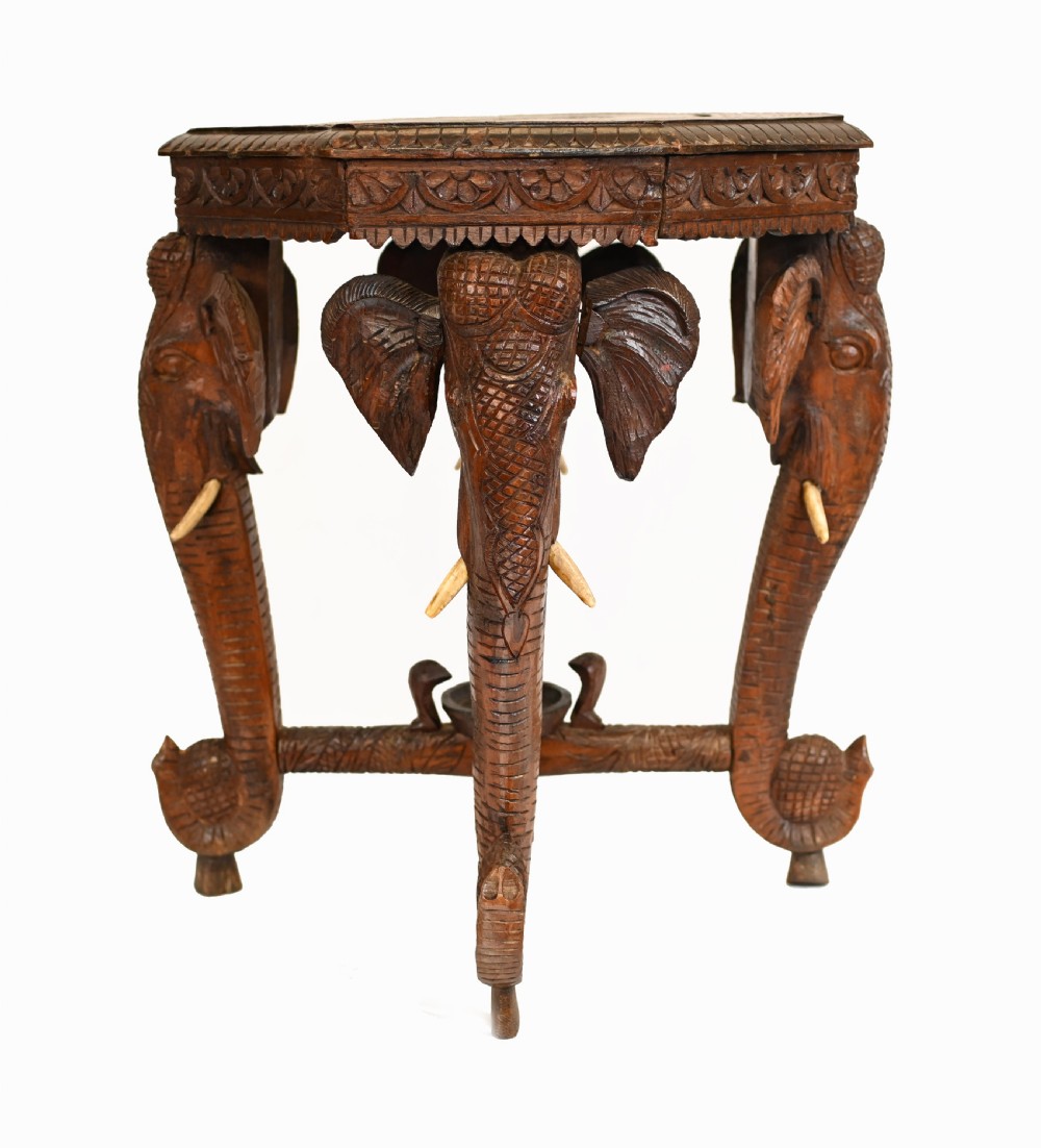 An octagonal carved wooden side table featuring three legs sculpted in the shape of elephant heads with trunks curving down to form the feet. View VIII