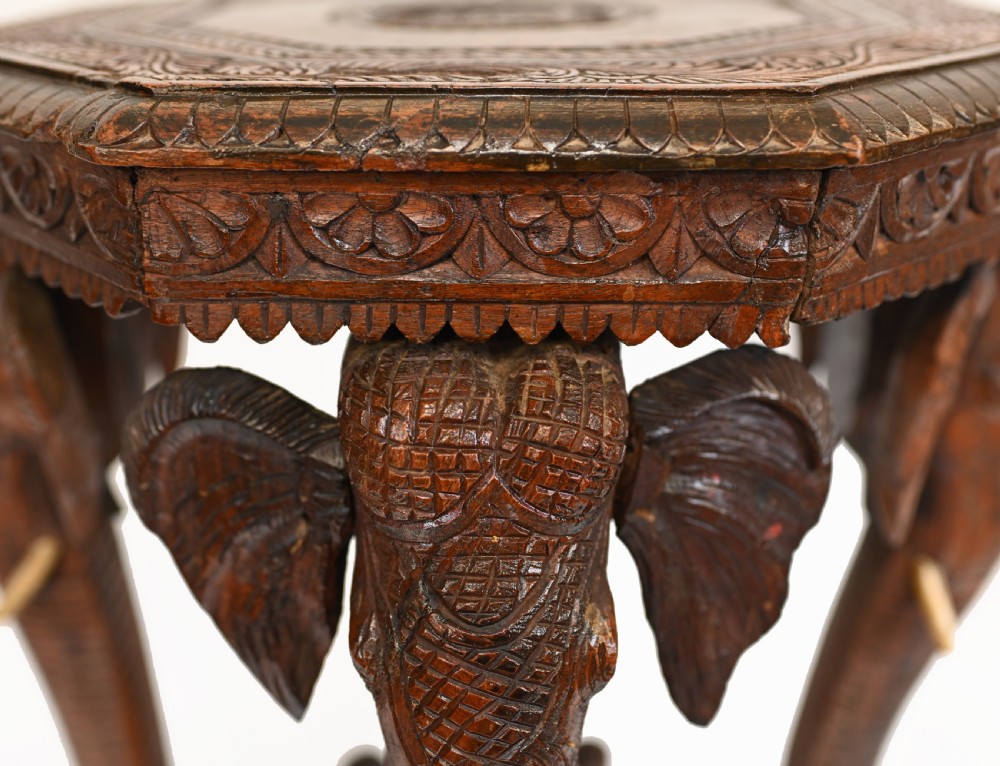 An octagonal carved wooden side table featuring three legs sculpted in the shape of elephant heads with trunks curving down to form the feet. View IX