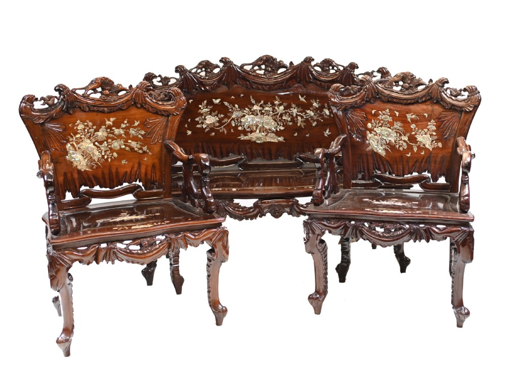 A three-piece dark hardwood seating suite comprising a double bench and two armchairs, decorated with mother of pearl floral inlays and carved detailing.