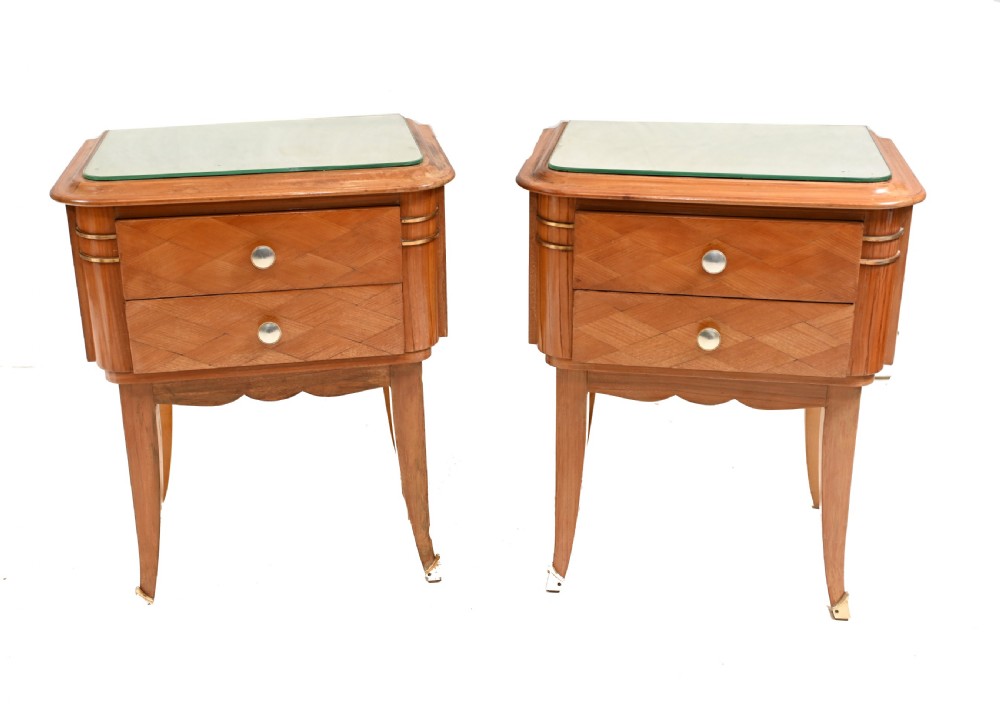 A pair of 1930s Art Deco wooden bedside cabinets featuring two drawers with diamond geometric veneers, rounded top edges with glass surface protectors, brass accents, and tapered legs.