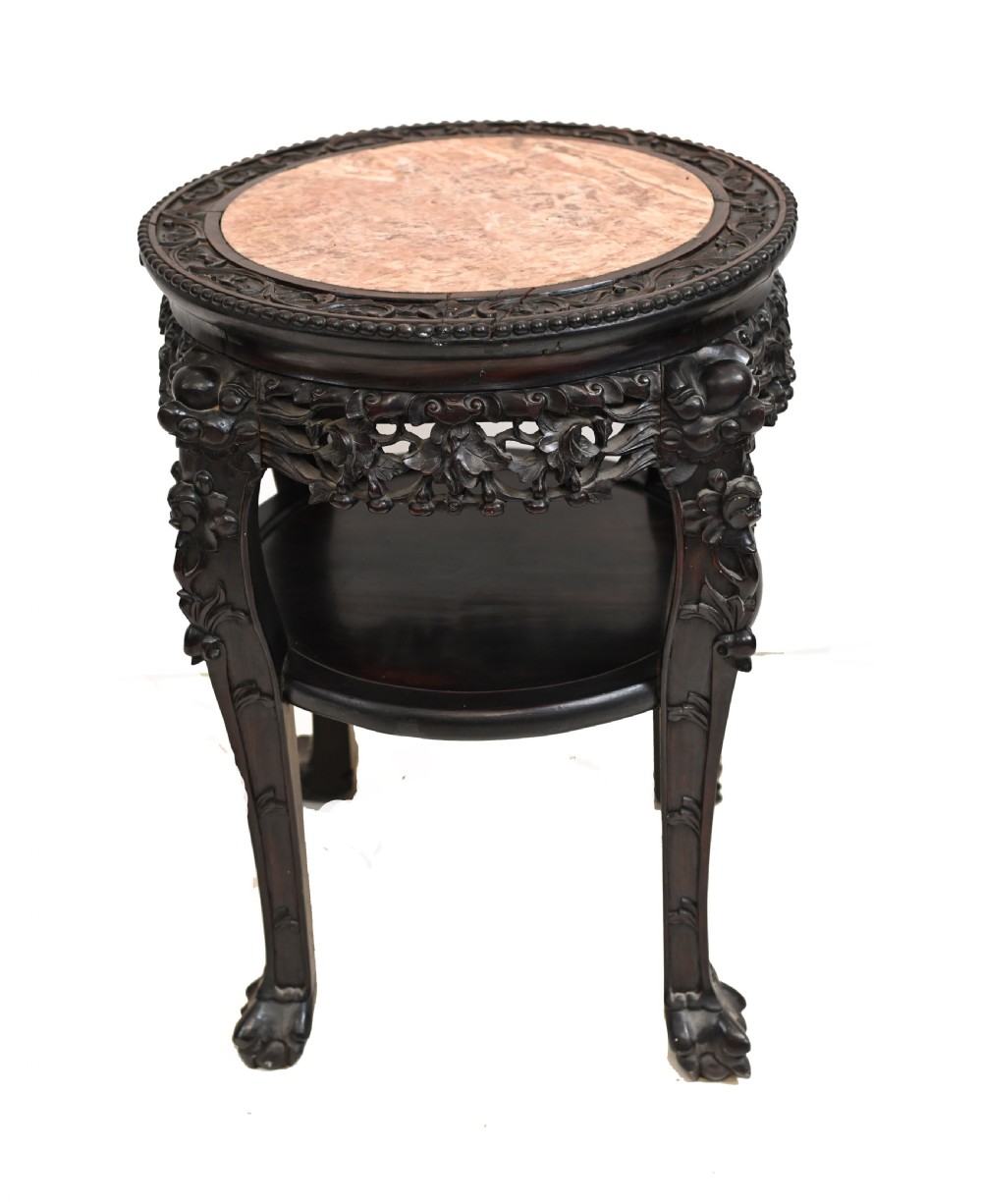 An antique Chinese dark hardwood side table featuring a circular inset marble top, openwork carved floral apron, lower tier, and carved legs.