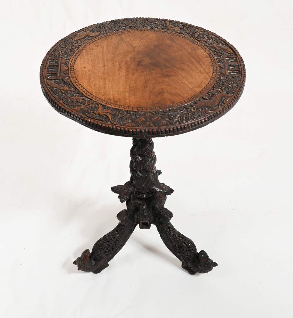 A circular 19th-century Burmese carved teak side table featuring intricate relief borders, a central plain top, a carved twisted stem, and tripod zoomorphic feet.