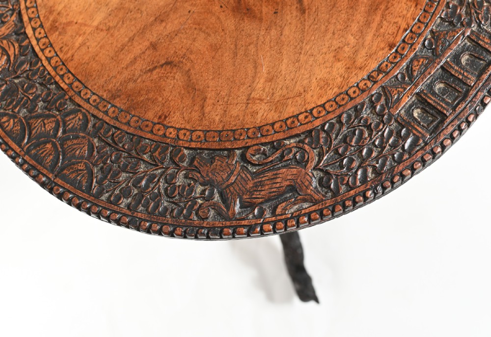A circular 19th-century Burmese carved teak side table featuring intricate relief borders, a central plain top, a carved twisted stem, and tripod zoomorphic feet. View VIII