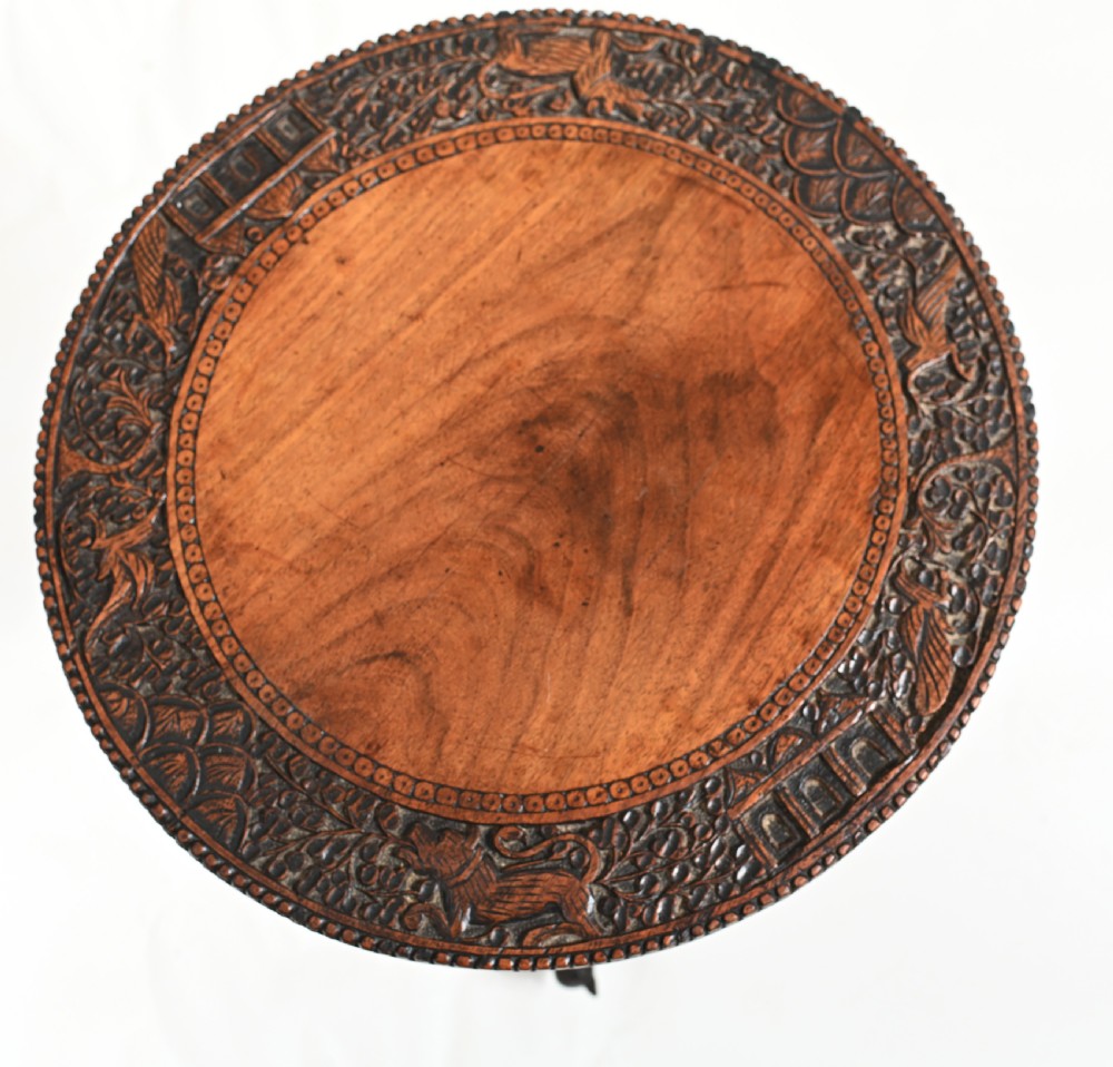 A circular 19th-century Burmese carved teak side table featuring intricate relief borders, a central plain top, a carved twisted stem, and tripod zoomorphic feet. View IX