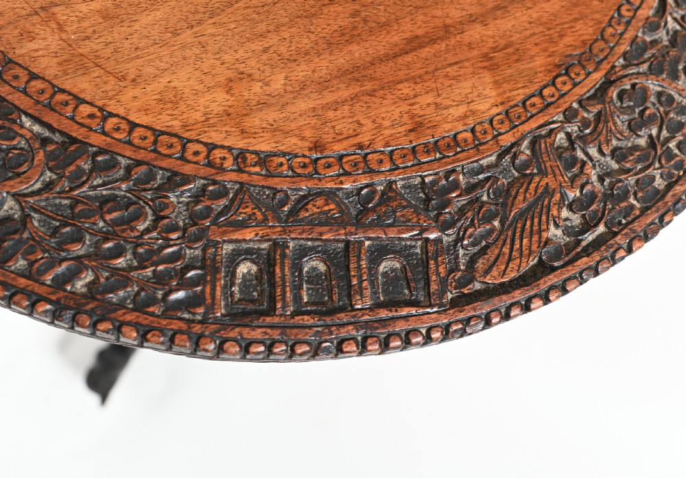 A circular 19th-century Burmese carved teak side table featuring intricate relief borders, a central plain top, a carved twisted stem, and tripod zoomorphic feet. View X