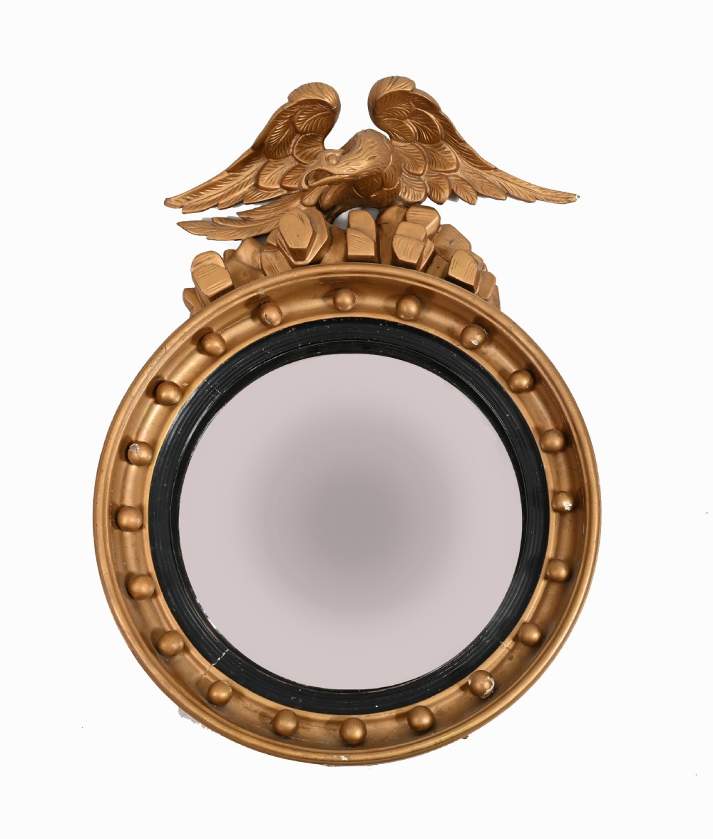 A circular Regency giltwood convex wall mirror topped with a carved eagle surmount and decorated with spherules around a black reeded slip.