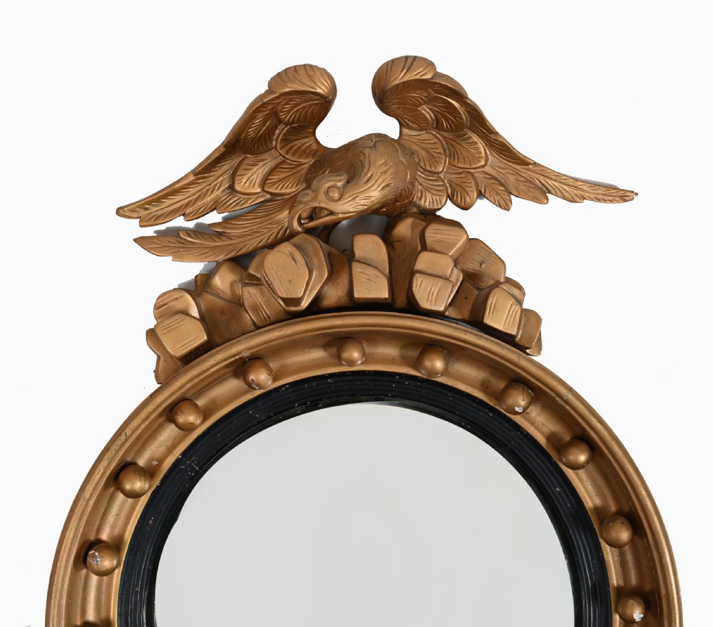 A circular Regency giltwood convex wall mirror topped with a carved eagle surmount and decorated with spherules around a black reeded slip. View II