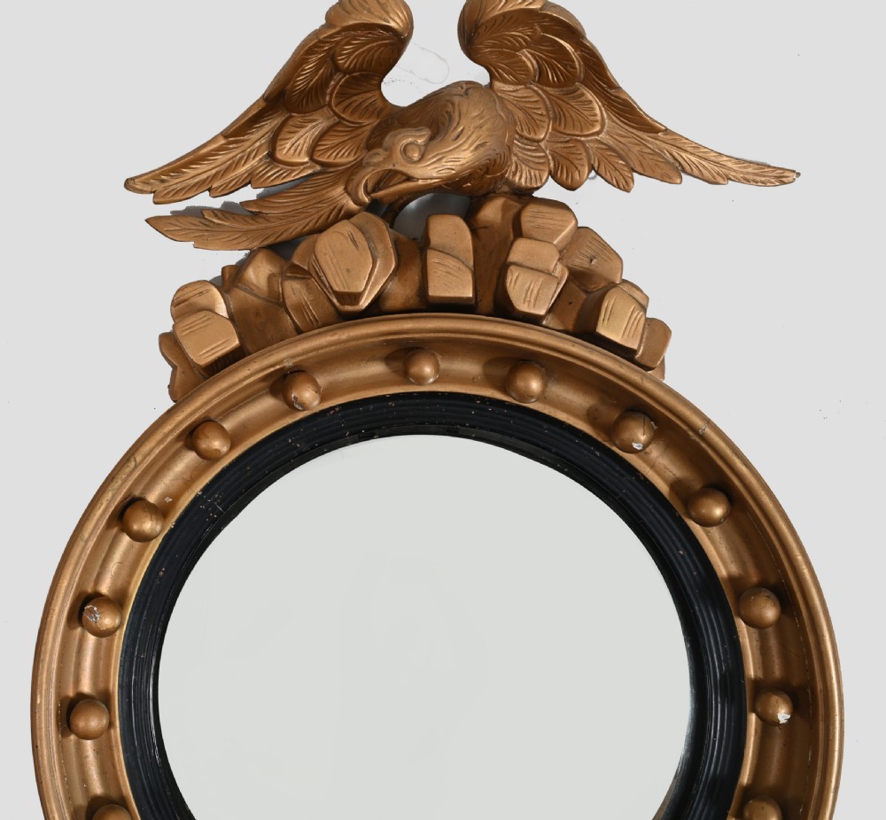 A circular Regency giltwood convex wall mirror topped with a carved eagle surmount and decorated with spherules around a black reeded slip. View III