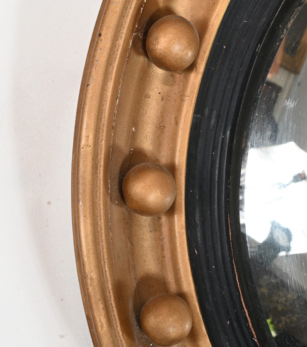 A circular Regency giltwood convex wall mirror topped with a carved eagle surmount and decorated with spherules around a black reeded slip. View IV