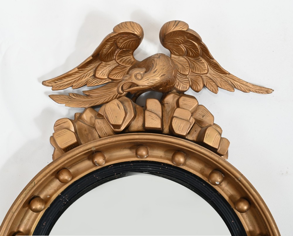 A circular Regency giltwood convex wall mirror topped with a carved eagle surmount and decorated with spherules around a black reeded slip. View V