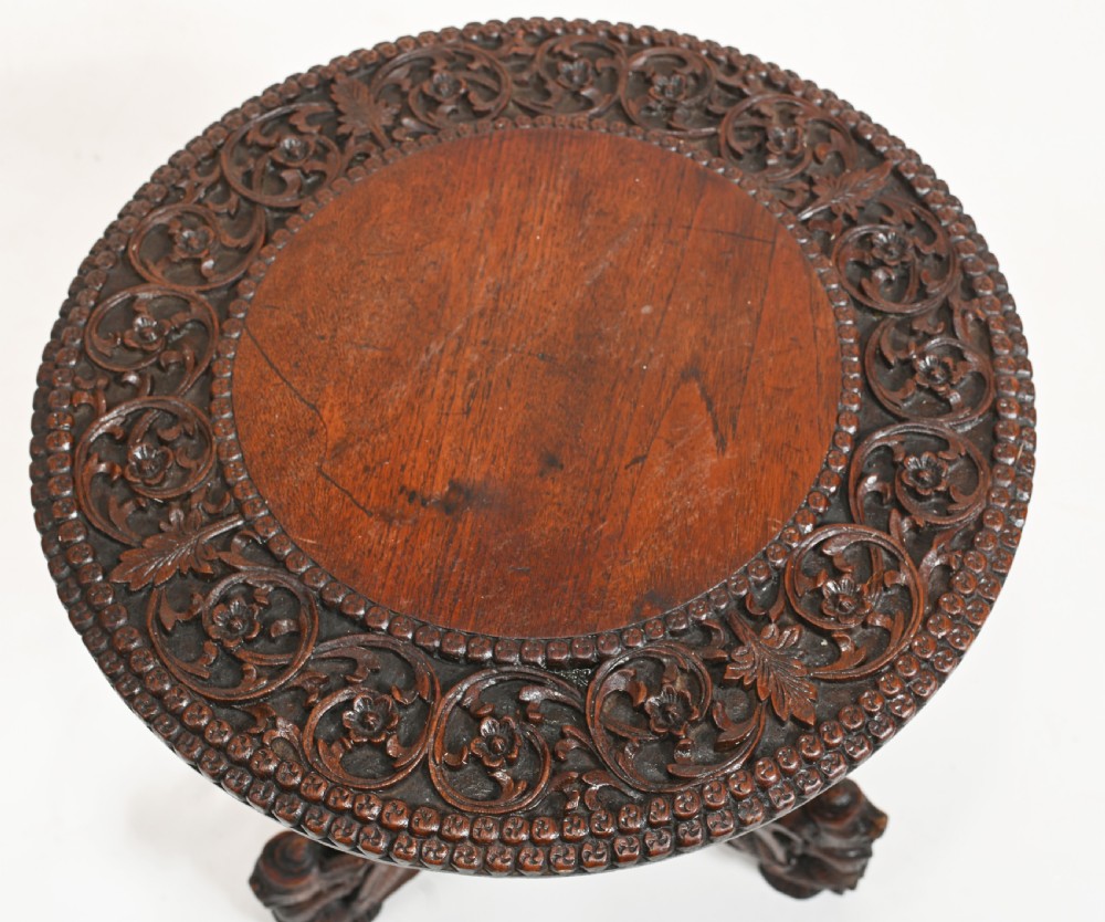 A dark brown carved timber side table featuring a circular top with a pierced floral border, supported on a turned stem and tripod legs shaped like mythological beasts. View III