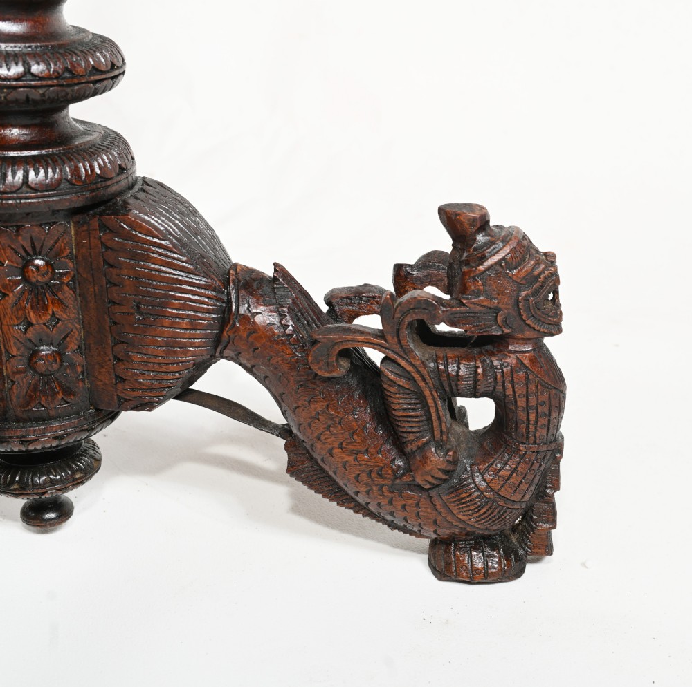 A dark brown carved timber side table featuring a circular top with a pierced floral border, supported on a turned stem and tripod legs shaped like mythological beasts. View VII