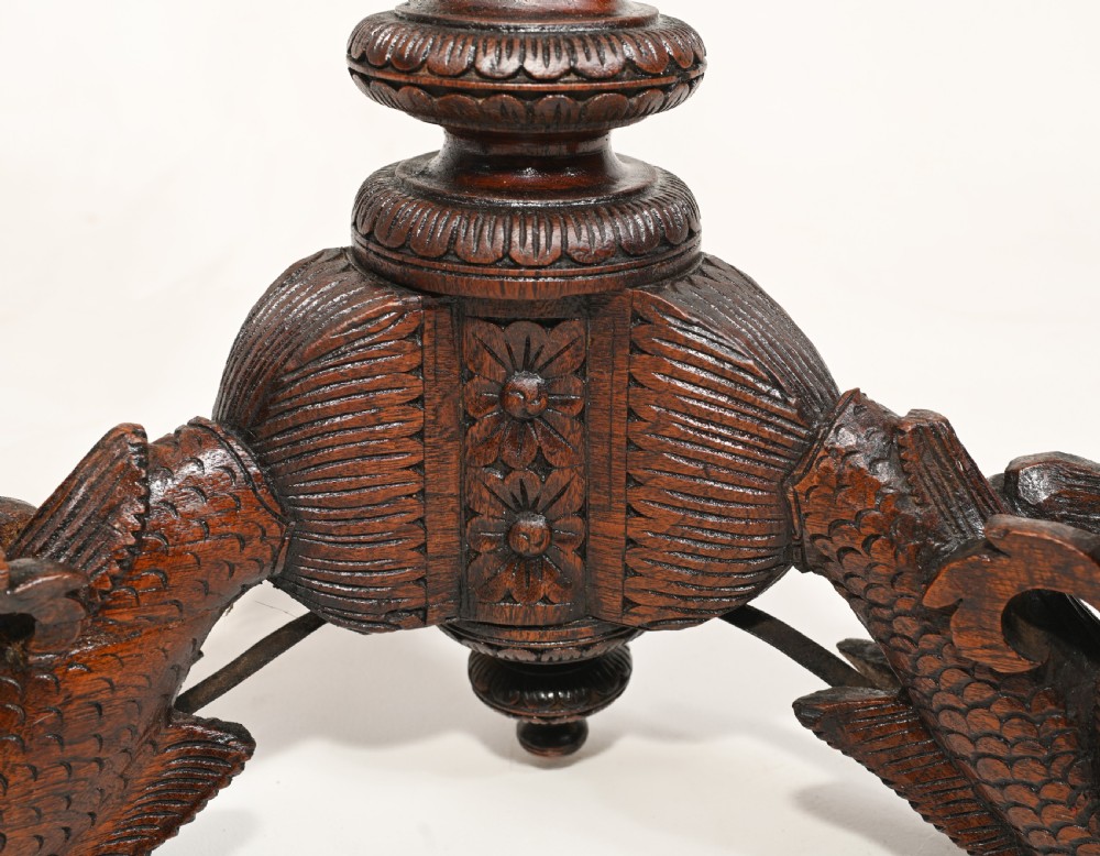 A dark brown carved timber side table featuring a circular top with a pierced floral border, supported on a turned stem and tripod legs shaped like mythological beasts. View IX