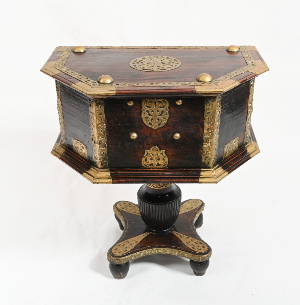 An antique dark wood Indian dowry casket decorated with intricate pierced brass straps and studs, supported on a turned central pedestal base. View II