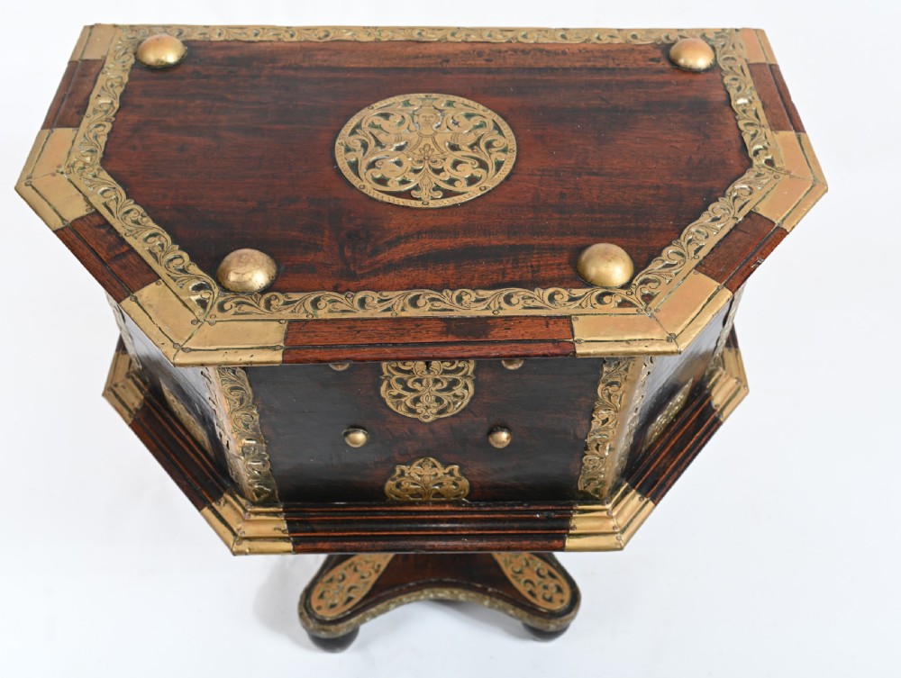 An antique dark wood Indian dowry casket decorated with intricate pierced brass straps and studs, supported on a turned central pedestal base. View III