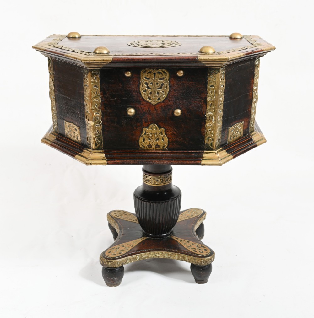 An antique dark wood Indian dowry casket decorated with intricate pierced brass straps and studs, supported on a turned central pedestal base. View V