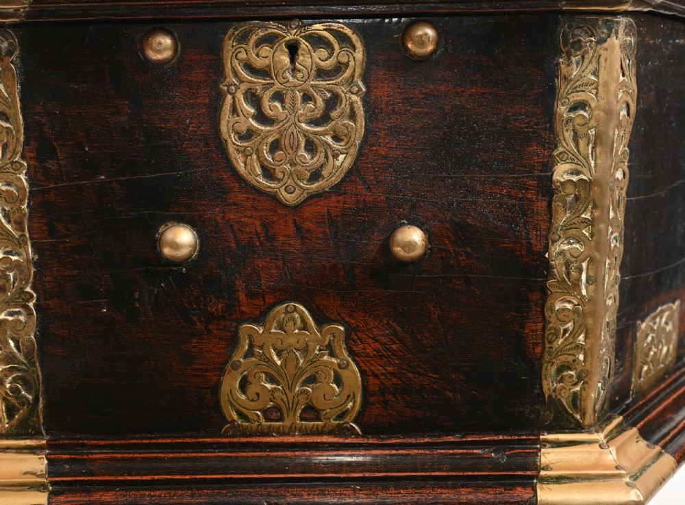 An antique dark wood Indian dowry casket decorated with intricate pierced brass straps and studs, supported on a turned central pedestal base. View VII