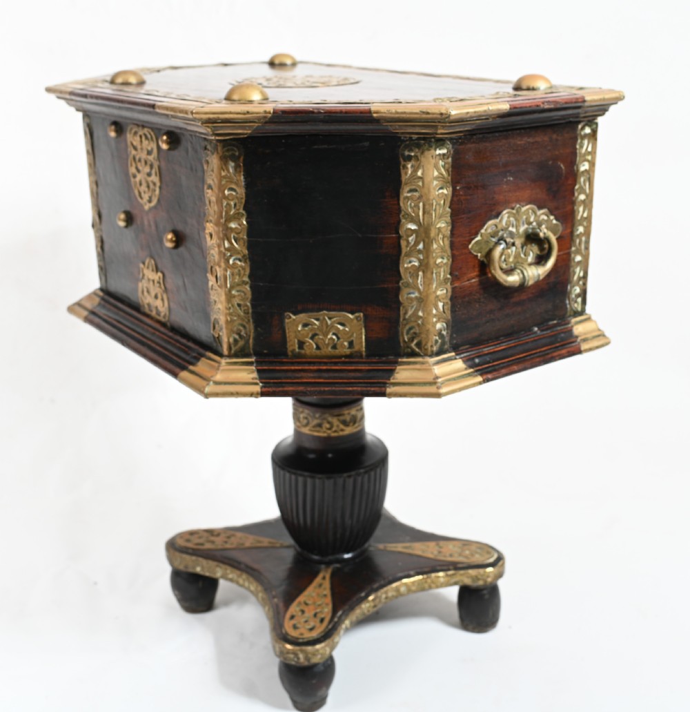 An antique dark wood Indian dowry casket decorated with intricate pierced brass straps and studs, supported on a turned central pedestal base. View VIII