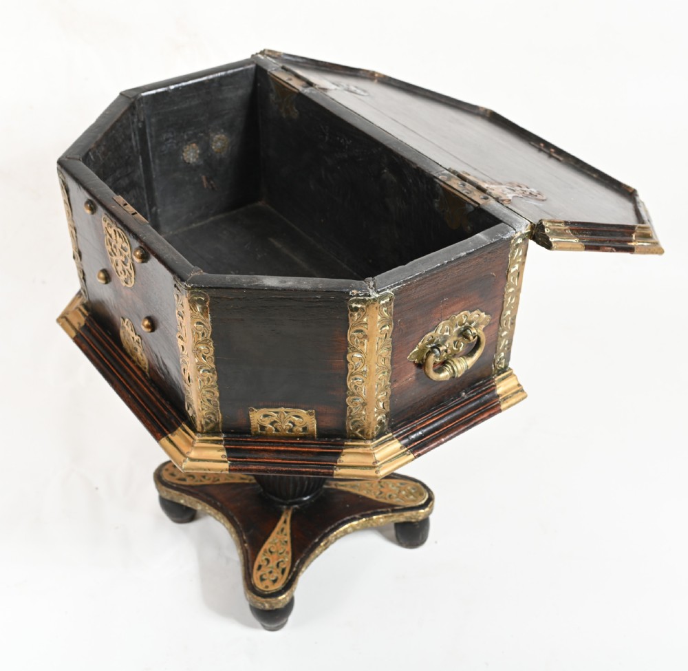 An antique dark wood Indian dowry casket decorated with intricate pierced brass straps and studs, supported on a turned central pedestal base. View IX