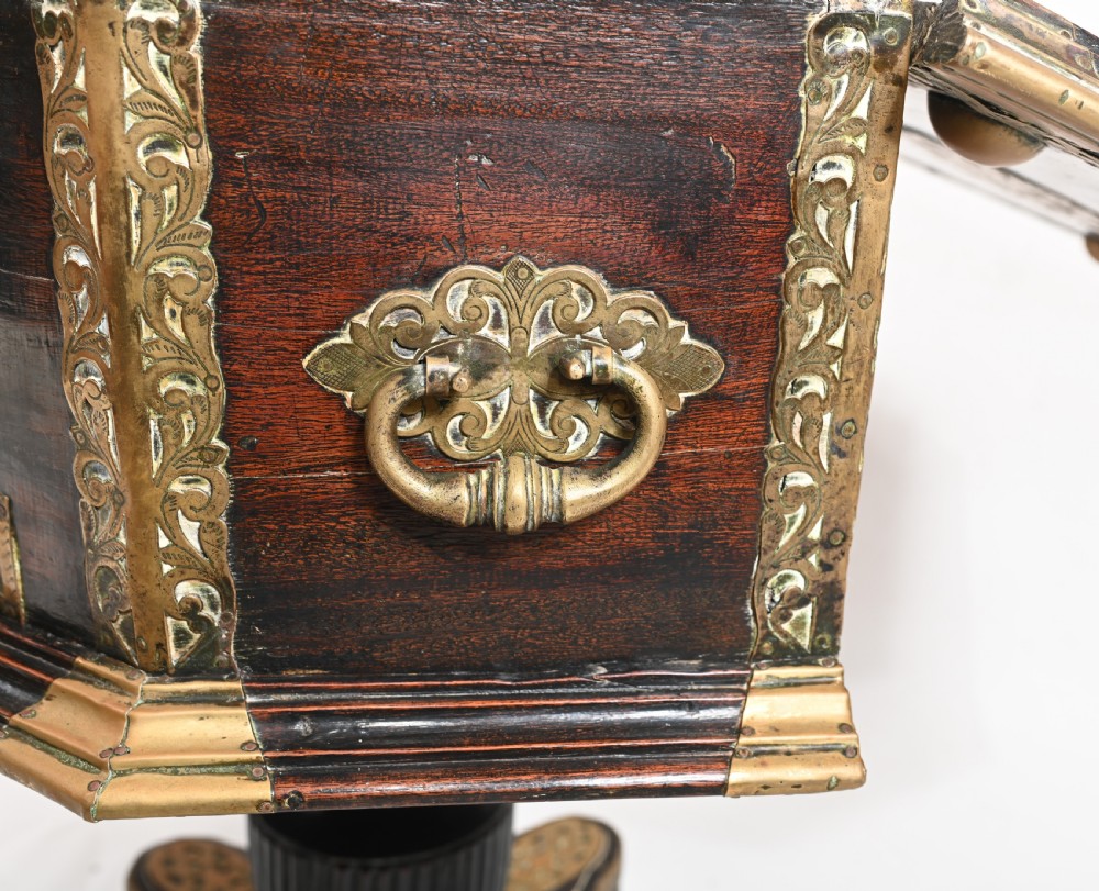 An antique dark wood Indian dowry casket decorated with intricate pierced brass straps and studs, supported on a turned central pedestal base. View X