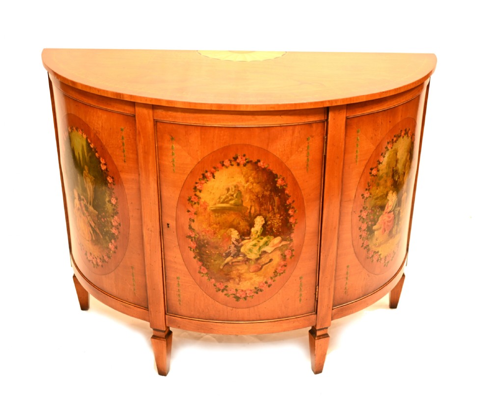 A semi-circular satinwood commode cabinet featuring three oval painted vignettes with classical figurative scenes and floral borders.