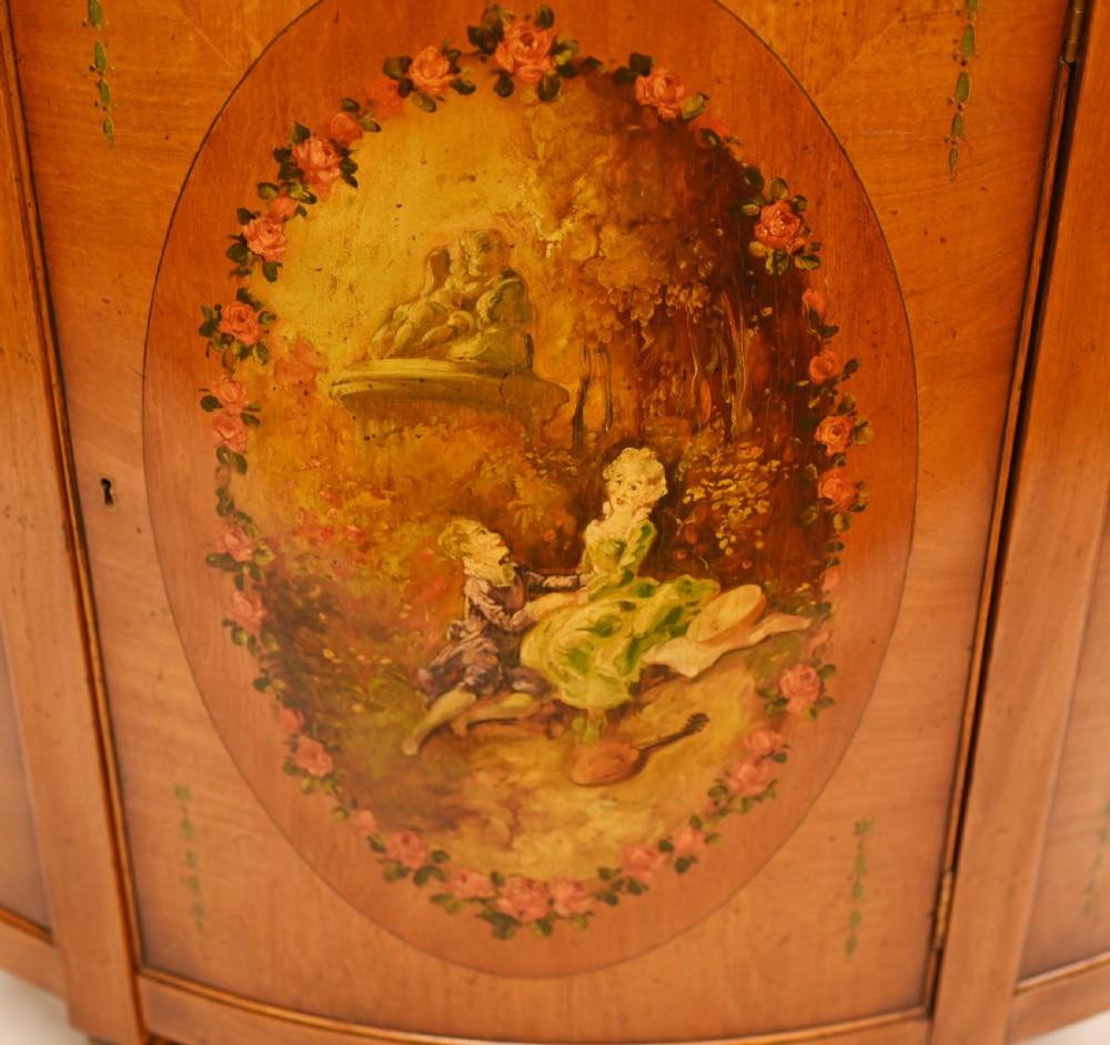 A semi-circular satinwood commode cabinet featuring three oval painted vignettes with classical figurative scenes and floral borders. View IV