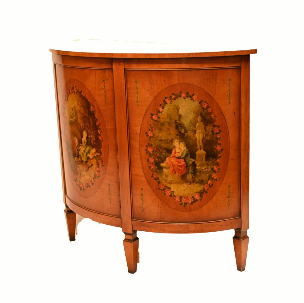 A semi-circular satinwood commode cabinet featuring three oval painted vignettes with classical figurative scenes and floral borders. View IX