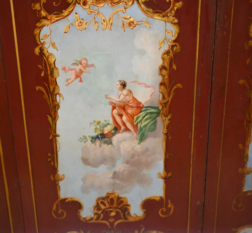 A red six-panel folding screen painted with classical figures, cherubs, and urns within gilded scrollwork borders. View V