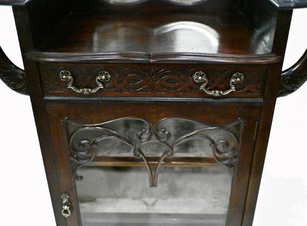 A dark mahogany Art Nouveau display cabinet featuring a pierced cresting, an asymmetrical mirrored superstructure, a single drawer, and a glazed door on slender shaped legs. View II