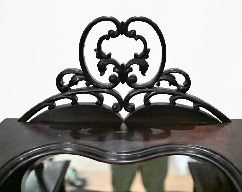 A dark mahogany Art Nouveau display cabinet featuring a pierced cresting, an asymmetrical mirrored superstructure, a single drawer, and a glazed door on slender shaped legs. View III